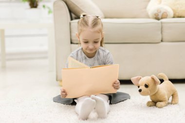 Yerde kitap okuyan küçük bir kız..