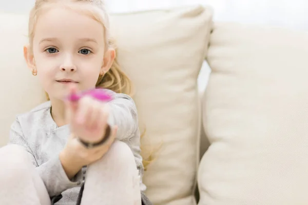 Niña bonita manteniendo una cuchara mientras se sienta en el sofá en un retrato de cerca. — Foto de Stock