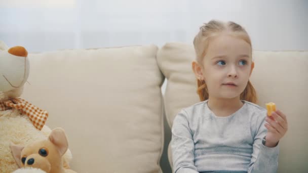 4k close up video de la pequeña hija rubia comiendo plátano y escuchando a alguien. — Vídeo de stock