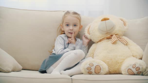 4k видео милой маленькой девочки делится секретами со своим плюшевым мишкой и улыбается. — стоковое видео