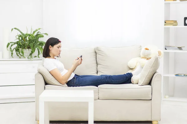 Foto der schönen Mutter liegt auf Sofa im Wohnzimmer und hält Telefon. — Stockfoto