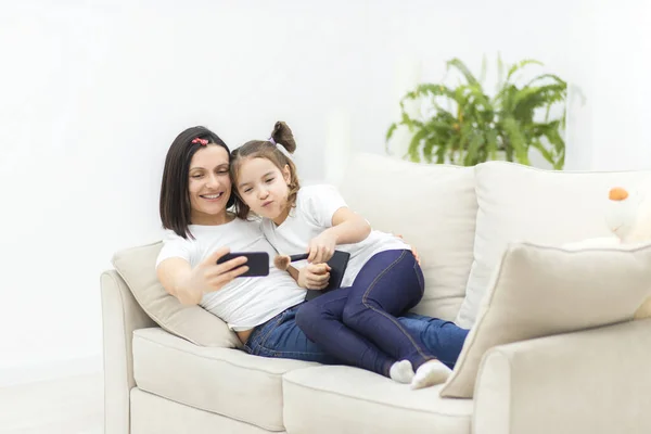 Szczęśliwa matka i córka siedzą na kanapie i robią selfie w salonie. — Zdjęcie stockowe