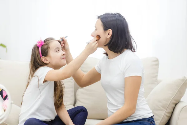 Pretty mother teaching her daughter doing make up at home.
