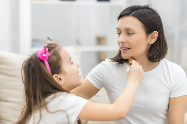 Linda madre enseñando a su hija haciendo maquillaje en casa. —  Fotos de Stock