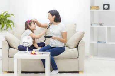 Genç ve güzel bir kadın aynanın yanında kızıyla makyaj yapıyor..