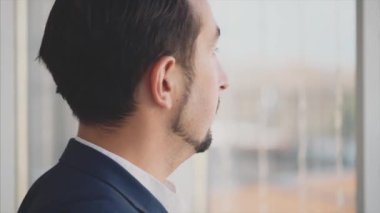 Resmi süitteki iş adamı şehir manzaralı panoramik pencerenin önünde duruyor. Ciddi bir adam. Profil görünümü. Dış profil. Kapatın. Animasyon. 4K.