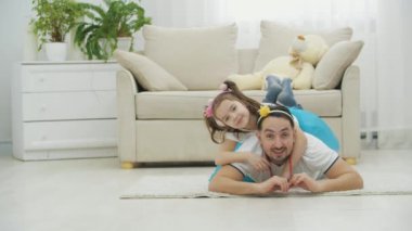 Güzel örgülü şirin küçük bir çocuk babasının sırtında yatıyor. Adam kadını yere atıyor ve ikisi de gülümsüyor..