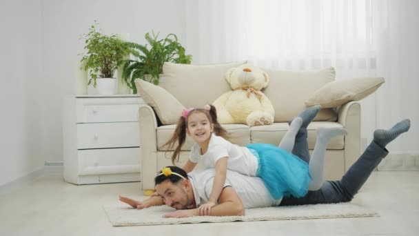 Jonge vader kruipt op de vloer tapijt met kleine dochter prinses op zijn rug. — Stockvideo