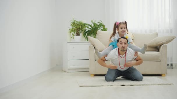 Vader zit op de grond, kleine dochter zit op zijn schouders in gespleten positie. — Stockvideo