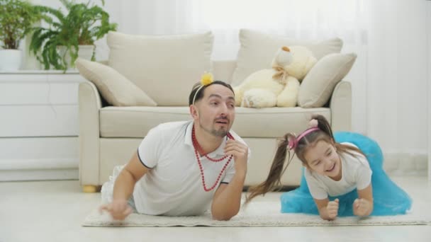 Vtipný otec pózuje na podlaze, ukazuje náhrdelník, pak dává pět svých krásných dcerušek, které se válejí na podlaze vedle něj. — Stock video