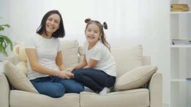 Annesi ve küçük kızının beyaz koltukta oturup bir video için poz verdiklerini gösteren 4K yavaş çekim videosu..