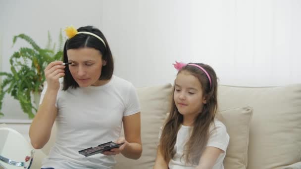 4k видео мать и ее милая дочь делают макияж вместе сидя на белом диване. — стоковое видео
