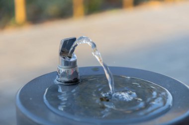 Halka açık bir çeşmeden akan suyun krom püskürtülmüş hali, açık ortamlardaki temel su ve temiz suya erişimi vurguluyor.