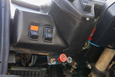 Turuncu uçlu sis lambası ve tehlike uyarısı düğmelerini gösteren rustik bir aracın detaylı yakın çekimi, ve kırmızı acil durum kolu.