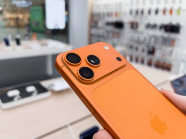 Poznan, Polonya - 20 Eylül 2025: iPhone 17 Pro, canlı turuncu, elinde, parlak bir elektronik perakende mağazası içinde üçlü kamera sistemini vurguluyor