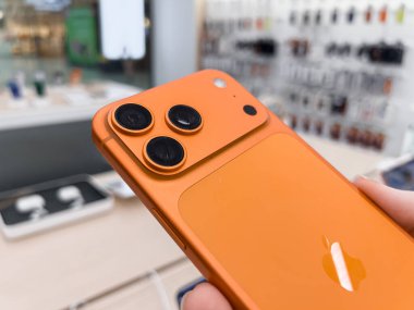 Poznan, Polonya - 20 Eylül 2025: Vibrant orange iPhone 17 Pro, modern bir elektronik mağazasında tutulan gelişmiş üçlü kamera sisteminin altını çiziyor