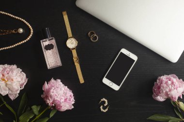Altın mücevherler, telefon ve dizüstü bilgisayar dairesi siyah arka planda yatıyordu - yüzük, tıknaz zincir kolye, saat, parfüm, küpeler, çiçekler