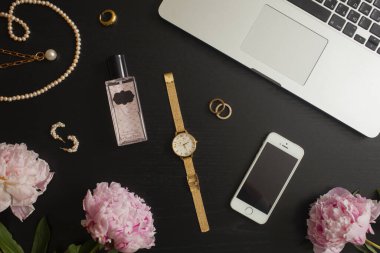 Altın mücevherler, telefon ve dizüstü bilgisayar dairesi siyah arka planda yatıyordu - yüzük, tıknaz zincir kolye, saat, parfüm, küpeler, çiçekler