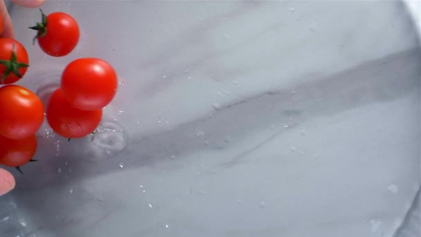 Tomaten fallen vor hellem Hintergrund ins Wasser. Zeitlupe — Stockvideo