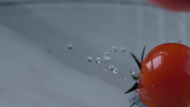 Os tomates caem na água sobre um fundo leve. Movimento lento — Vídeo de Stock