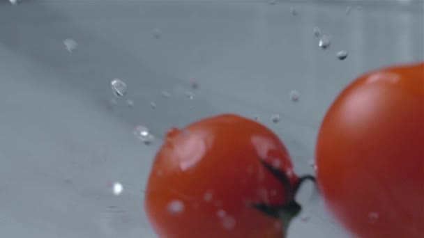 Tomater faller i vatten över en ljus bakgrund. Slow motion — Stockvideo