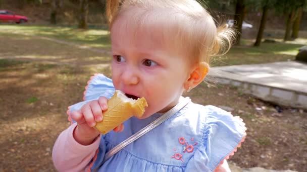 Portré egy kis szőke lány eszik fagylaltot a parkban. Lassított mozgás — Stock videók