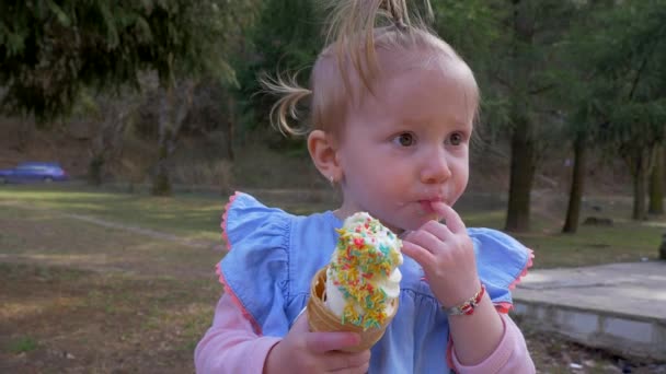Портрет маленькой блондинки, которая ест мороженое в парке. Медленное движение — стоковое видео