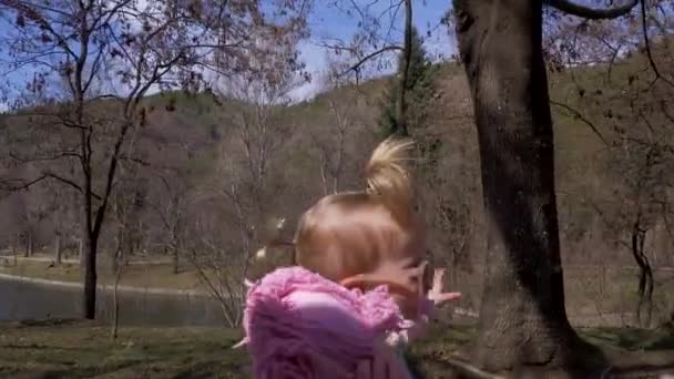 Ένα κοριτσάκι περπατάει στο πάρκο με γυαλιά ηλίου και κούκλα. Αργή κίνηση — Αρχείο Βίντεο