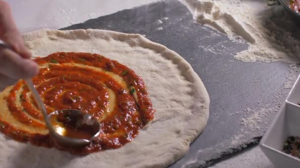 Een chef-kok zet een tomatensaus op de pizza — Stockvideo