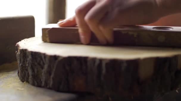 Le charpentier polit la planche en bois avec le papier de verre sur le bureau. — Video