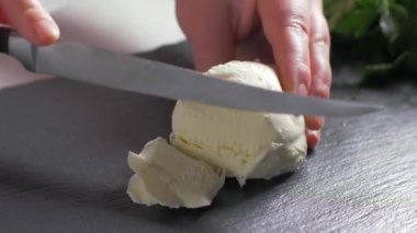 Kadın elleri mozzarella peynirini taşa kesiyor. Siyah arka plan