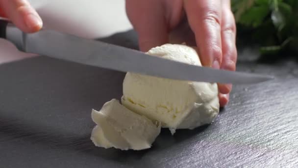 女性の手が石の上にモッツァレラチーズをカット。黒の背景 — ストック動画