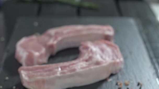 Сировина свиняча відбивна з кісткою. Розмарі падає на сире м'ясо. — стокове відео