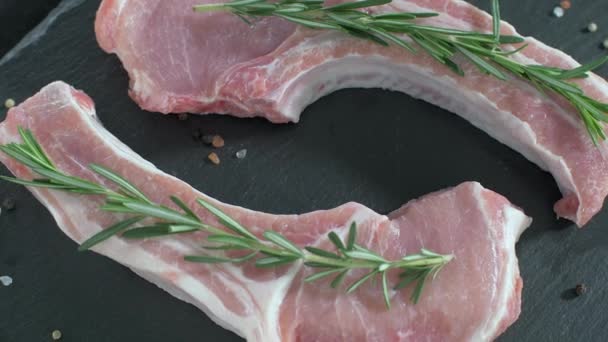 Syrové vepřové kotlety s kostí. Rosemary padá na syrové maso. — Stock video