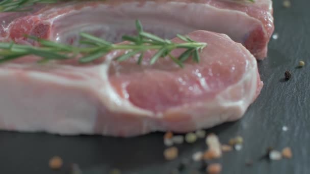 Rauwe Varkenskarbonades met bot. Rozemarijn valt op rauw vlees. — Stockvideo