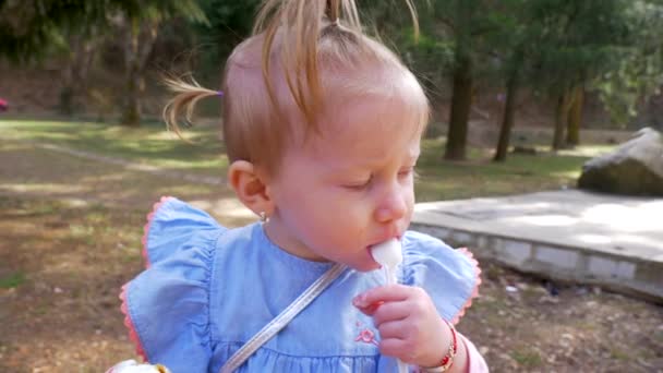 Портрет маленької блондинки, яка їсть морозиво в парку. Повільний рух — стокове відео