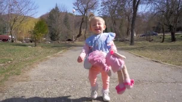 A menina caminha no parque com boneca. Movimento lento — Vídeo de Stock
