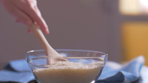 Женщина берет рис Басмати с деревянной ложкой из миски — стоковое видео