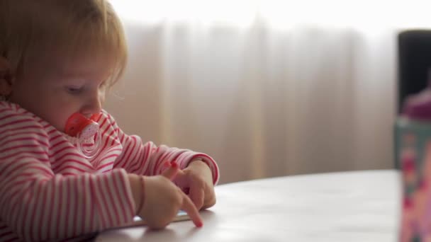 A little girl with a pacifier playing with a phone — Stock Video