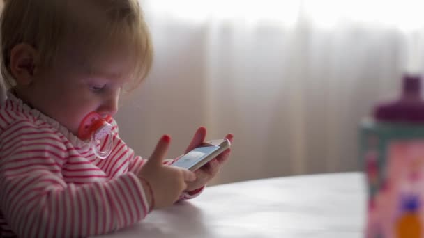 Een klein meisje met een fopspeen spelen met een telefoon — Stockvideo