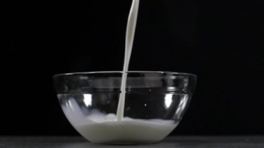 Cam bir kaseye taze süt döküyor. Siyah arka plan