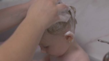 Çekici iki yaşındaki kız banyo alır. Anne bir şampuan ile saç temiz.