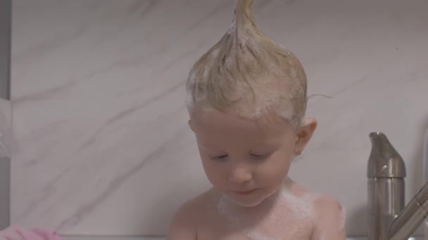 Aantrekkelijk twee jaar oud meisje neemt een bad. Moeder schoon haar met een shampoo. — Stockvideo