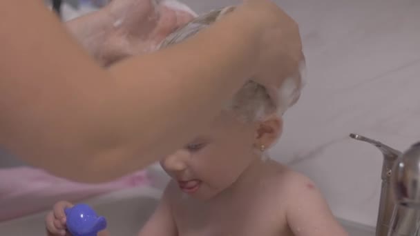 Attraktives zweijähriges Mädchen badet. Mama saubere Haare mit Shampoo. — Stockvideo