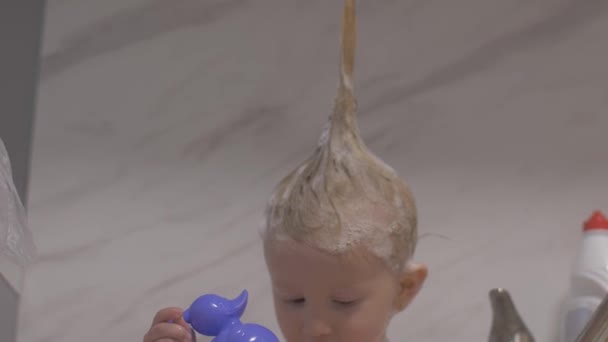 Atractiva niña de dos años toma un baño. Mamá limpia el cabello con un champú . — Vídeos de Stock