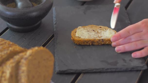 De hand verspreidde olie op een stuk volkoren brood op een zwarte steen — Stockvideo