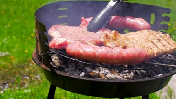 屋外のグリルプレートにソーセージとポークステーキを焼きます。グリル食品、バーベキュー — ストック動画