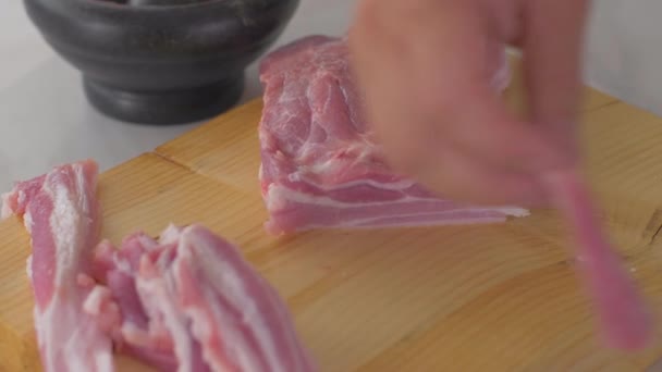 Chef corta trozos de tocino crudo con un cuchillo afilado en la tabla de madera — Vídeo de stock