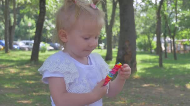 Linda niña rubia comiendo una piruleta en el parque — Vídeos de Stock