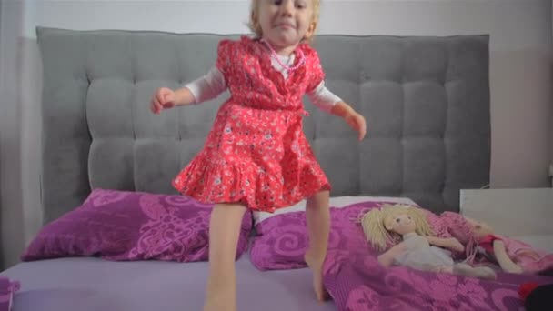 Счастливая блондинка в красном платье прыгает на кровати — стоковое видео